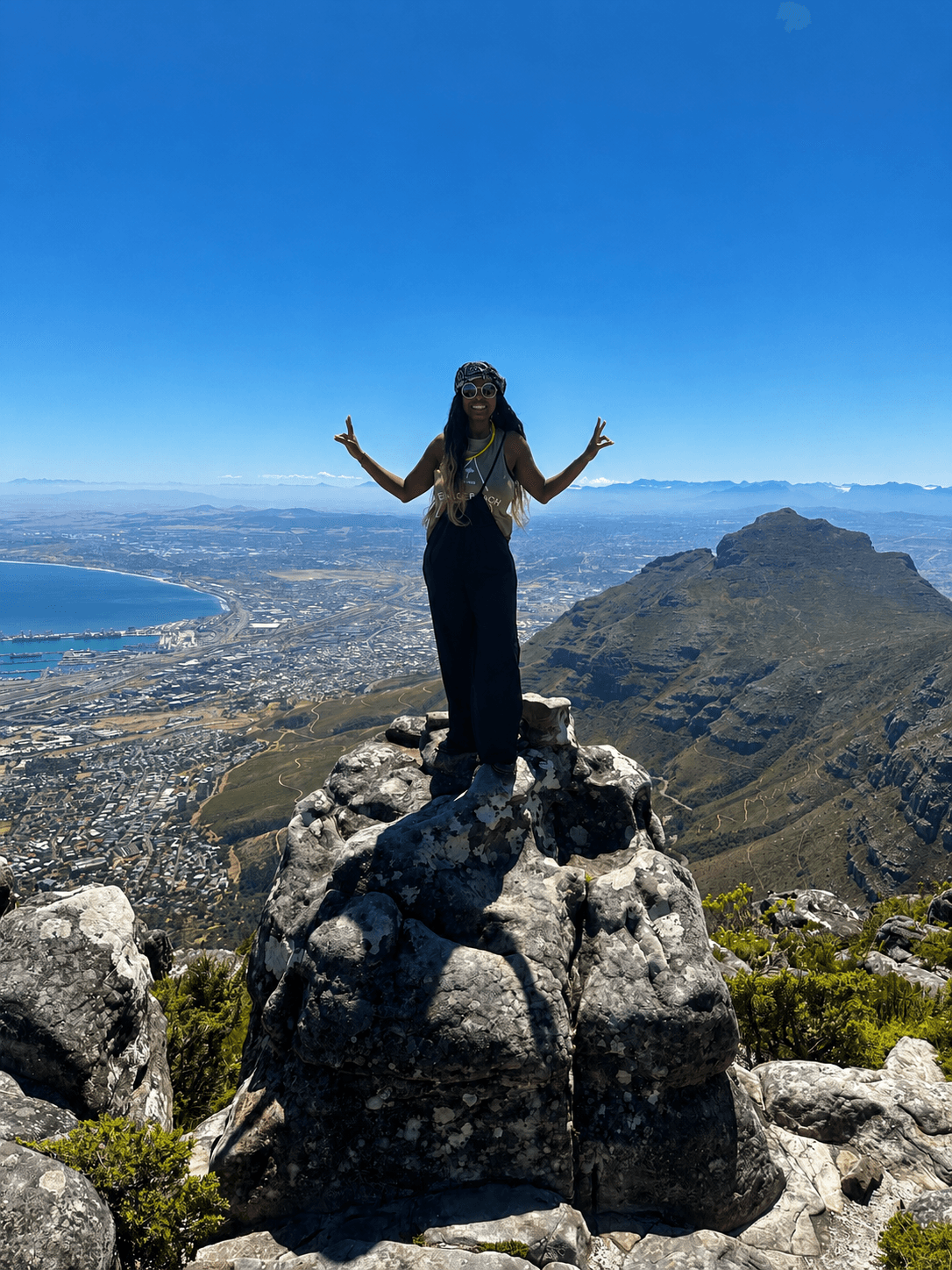 Solo traveller on a mountain summit overlooking a city and bay